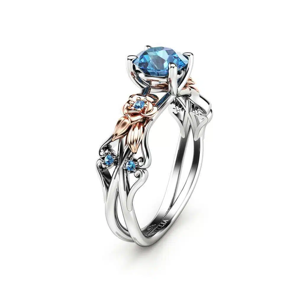 An angled view of a floral engagement ring featuring a blue diamond center and rose gold flower petals.