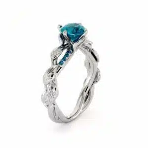 An angled view of a leaf-themed engagement ring featuring a blue diamond and twisting white gold band.