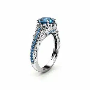 An angled view of a filigree engagement ring with a blue diamond center and scrollwork band.