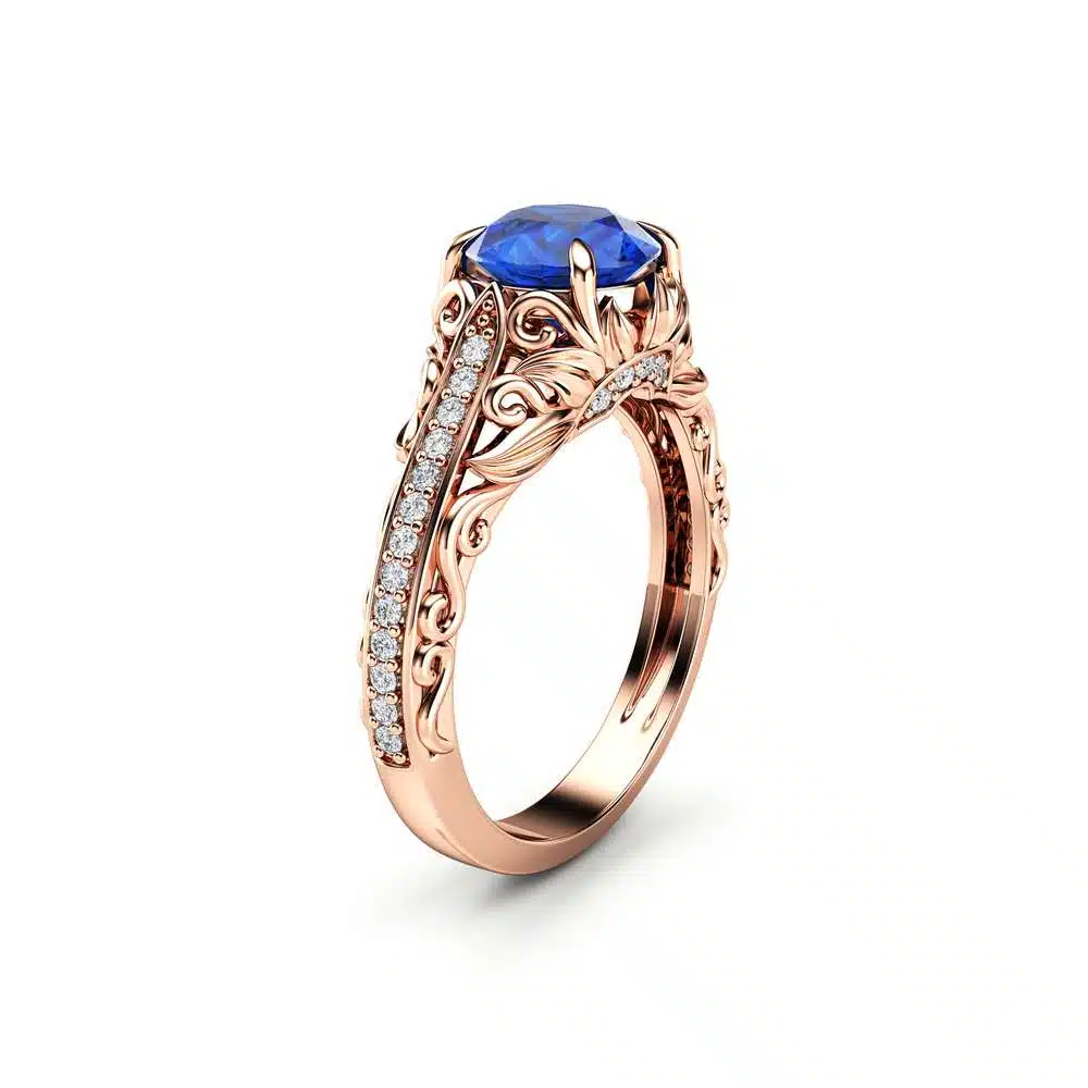 AL-0055C — Rose Gold, angled view Rose gold sapphire engagement ring at an angle, round blue sapphire in a scrolling filigree gallery with pave diamond shoulders