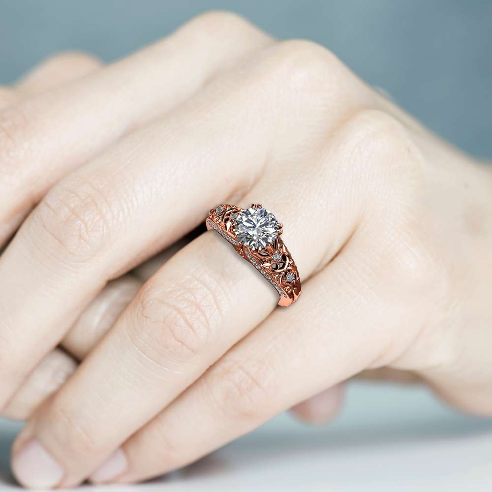 Rose gold vintage filigree engagement ring worn on the hand against a soft blue background
