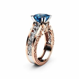 An angled view of an Art Deco engagement ring with a blue diamond center and two-tone floral filigree.