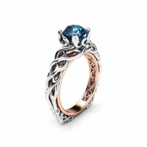 An angled view of a braided Celtic engagement ring with a blue diamond center.