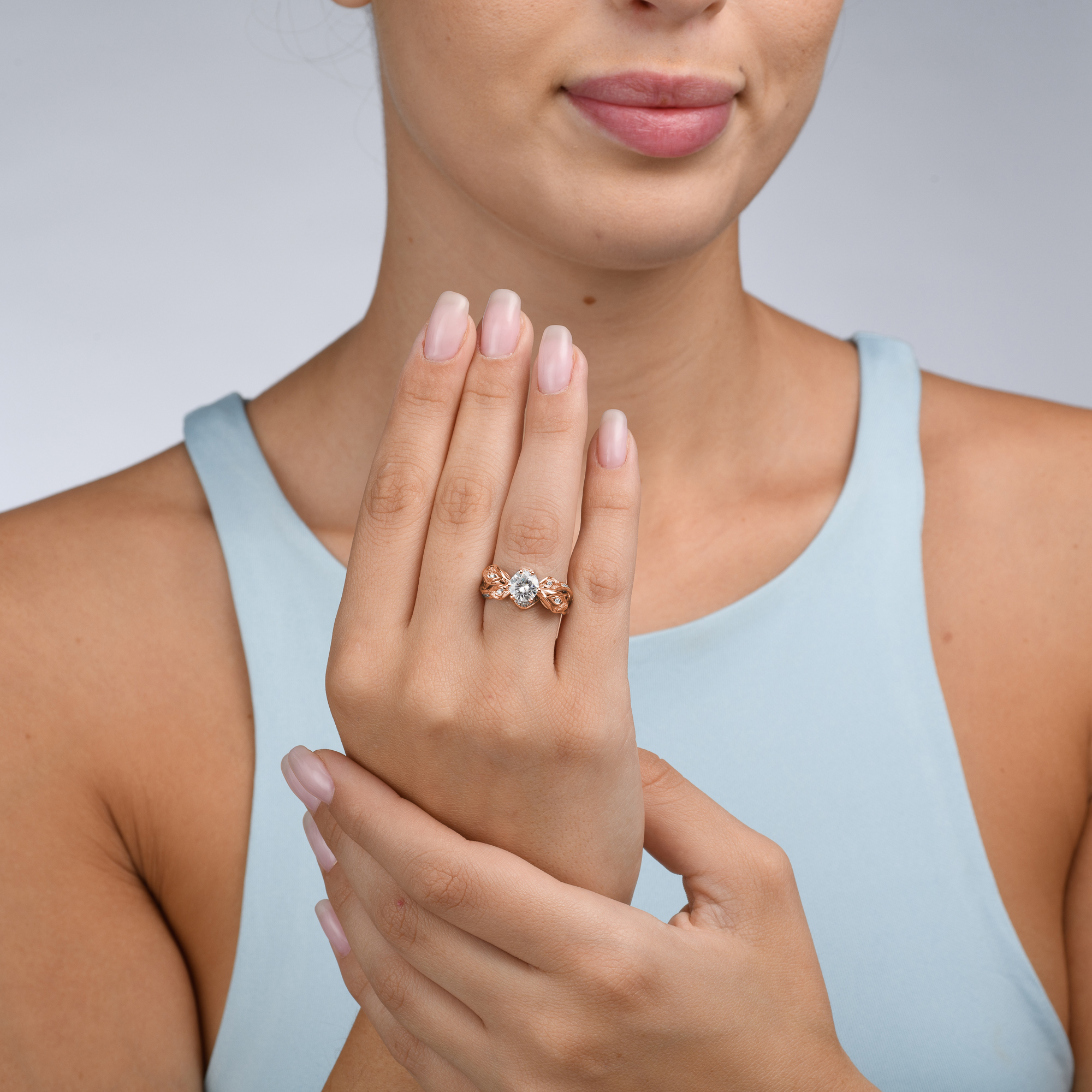CD-0001A — Rose Gold, worn on hand Woman wearing the rose gold calla lily moissanite ring, hand raised to her collarbone over a pale blue top