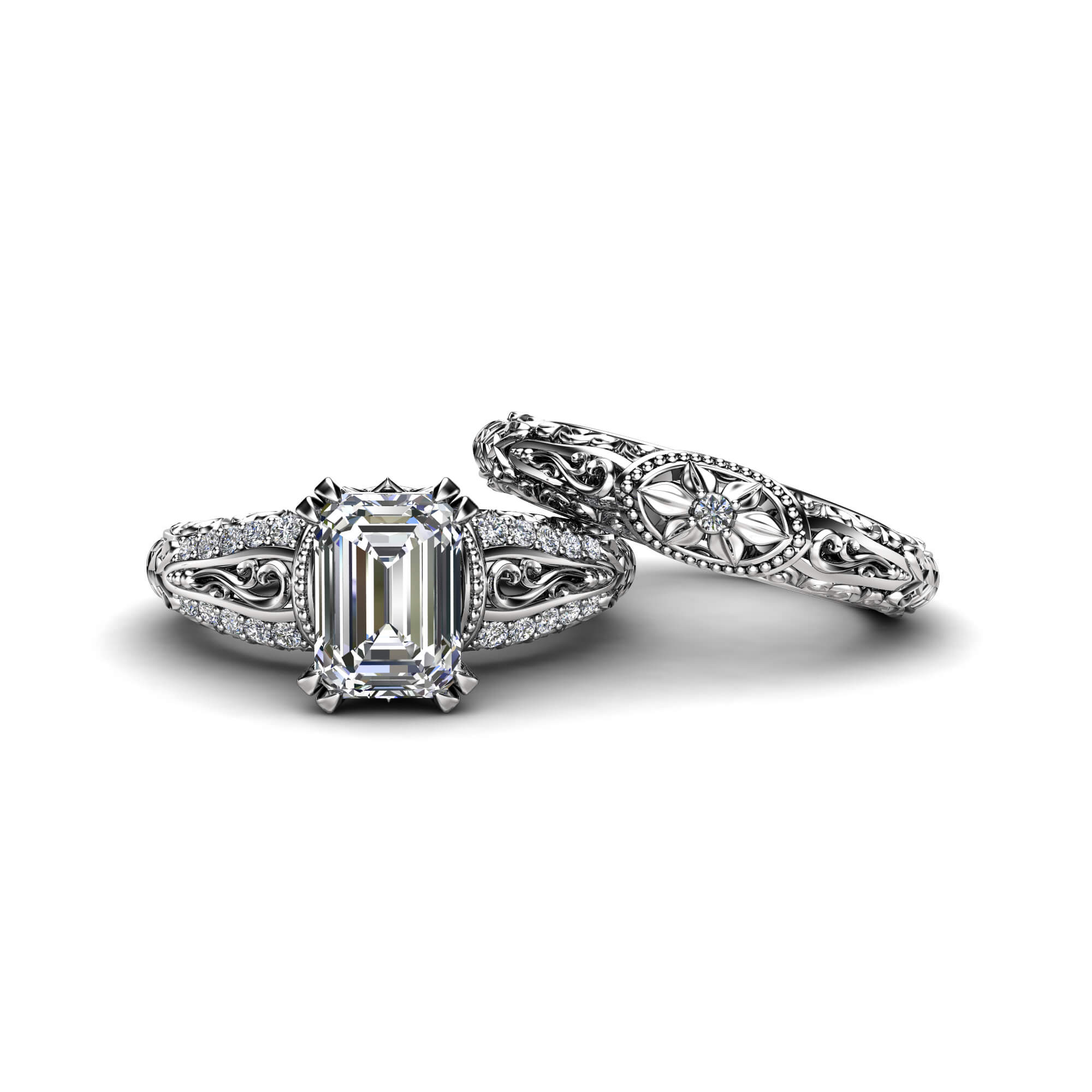 Side-by-Side Emerald Engagement Ring and Band Separate view of an emerald-cut diamond engagement ring and a matching filigree floral wedding band.
