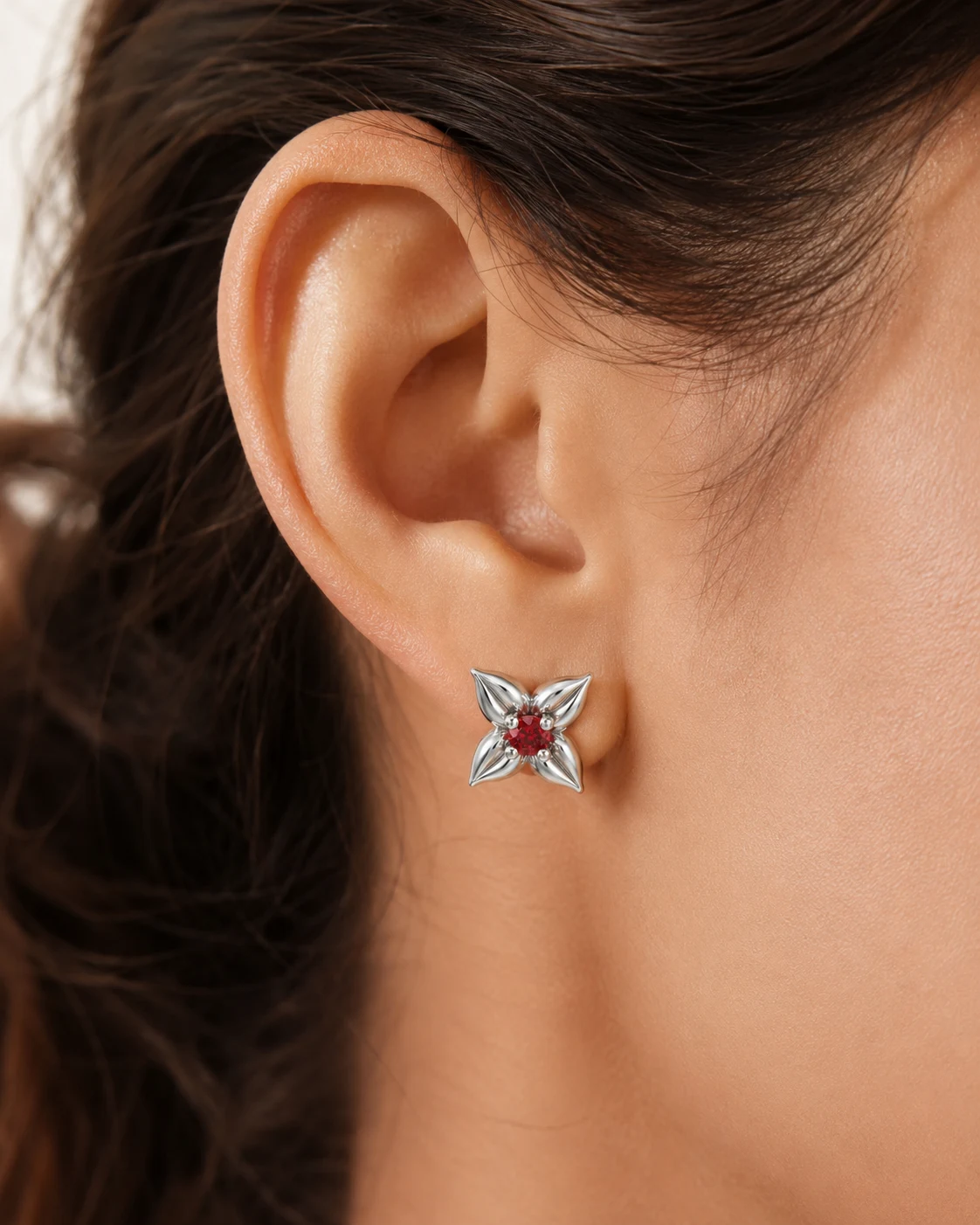AR-0001H-SO — White Gold, worn on ear White gold ruby flower stud worn on the ear, its sculpted petals framing a small round red ruby